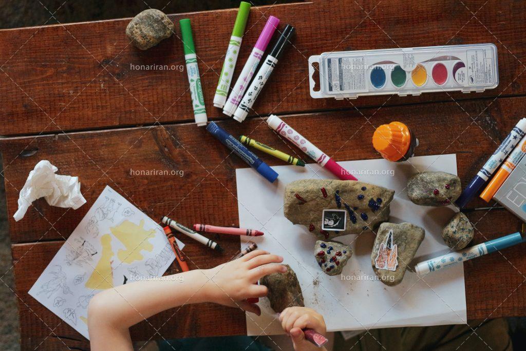 عکس با کیفیت کودک در حال رنگ آمیزی سنگ ها