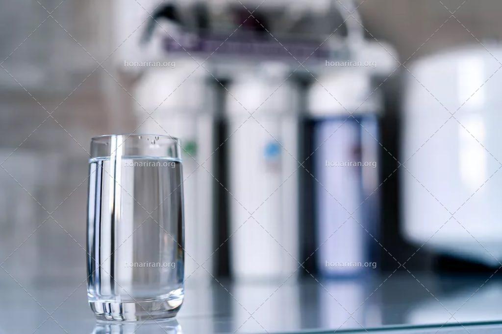 عکس با کیفیت لیوان آب در کنار دستگاه تصفیه آب