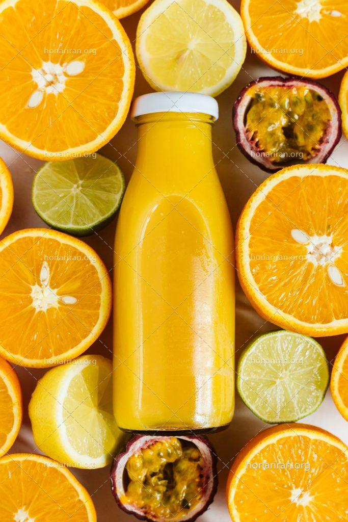عکس با کیفیت برش های پرتقال و لیمو در کنار شیشه آبمیوه