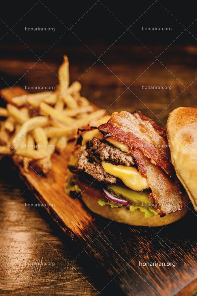 عکس با کیفیت ساندویچ همبرگر و بیکن در کنار سیب زمینی ها