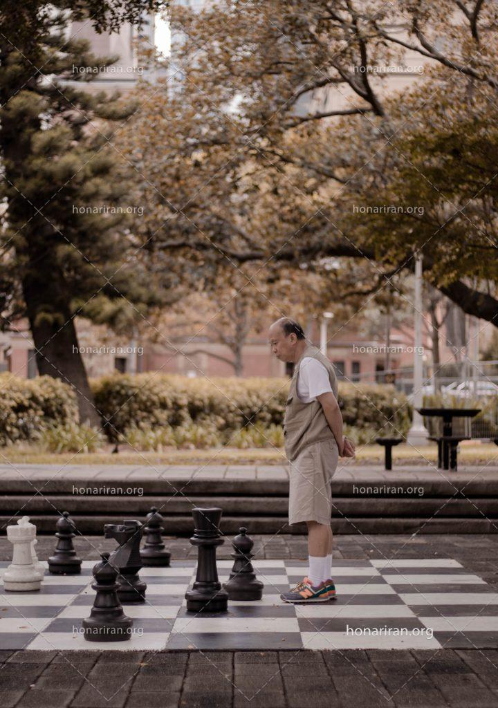 عکس با کیفیت پیرمرد ایستاده در کنار المان شطرنج