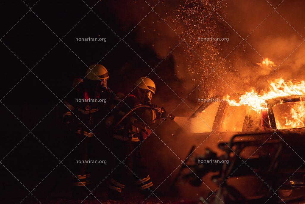 عکس با کیفیت ماشین آتش گرفته و آتش نشان ها در حال خاموش کردن آتش