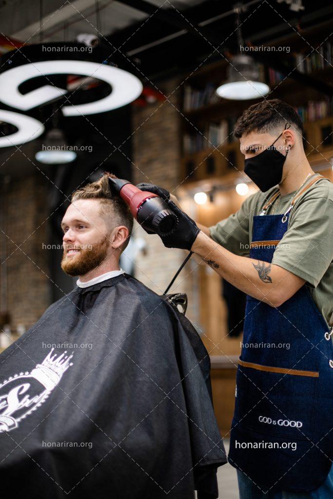 عکس با کیفیت آرایشگر در حال سشوار کردن موهای مرد