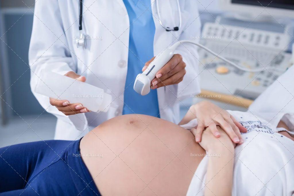 عکس با کیفیت پزشک در حال ریختن ژل بر روی شکم زن باردار